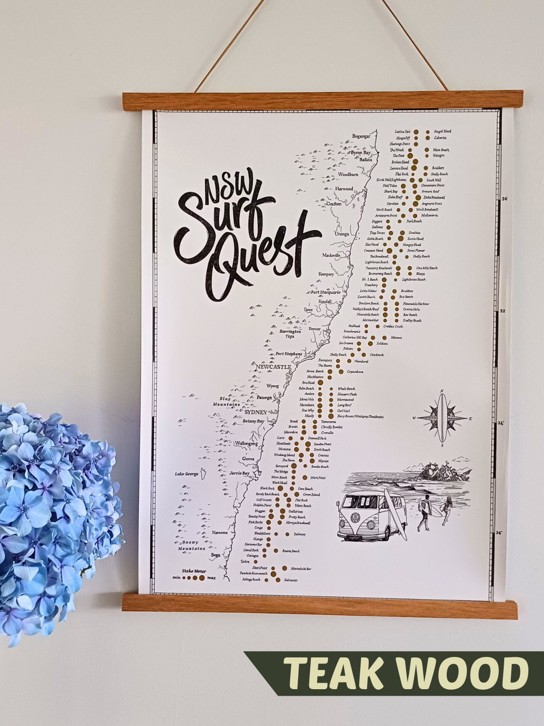 NSW Surf Quest Scratch Map displayed in a teak wood magnetic poster hanger, hanging on a wall with blue hydrangeas beside it, stylish home decor for surf lovers.