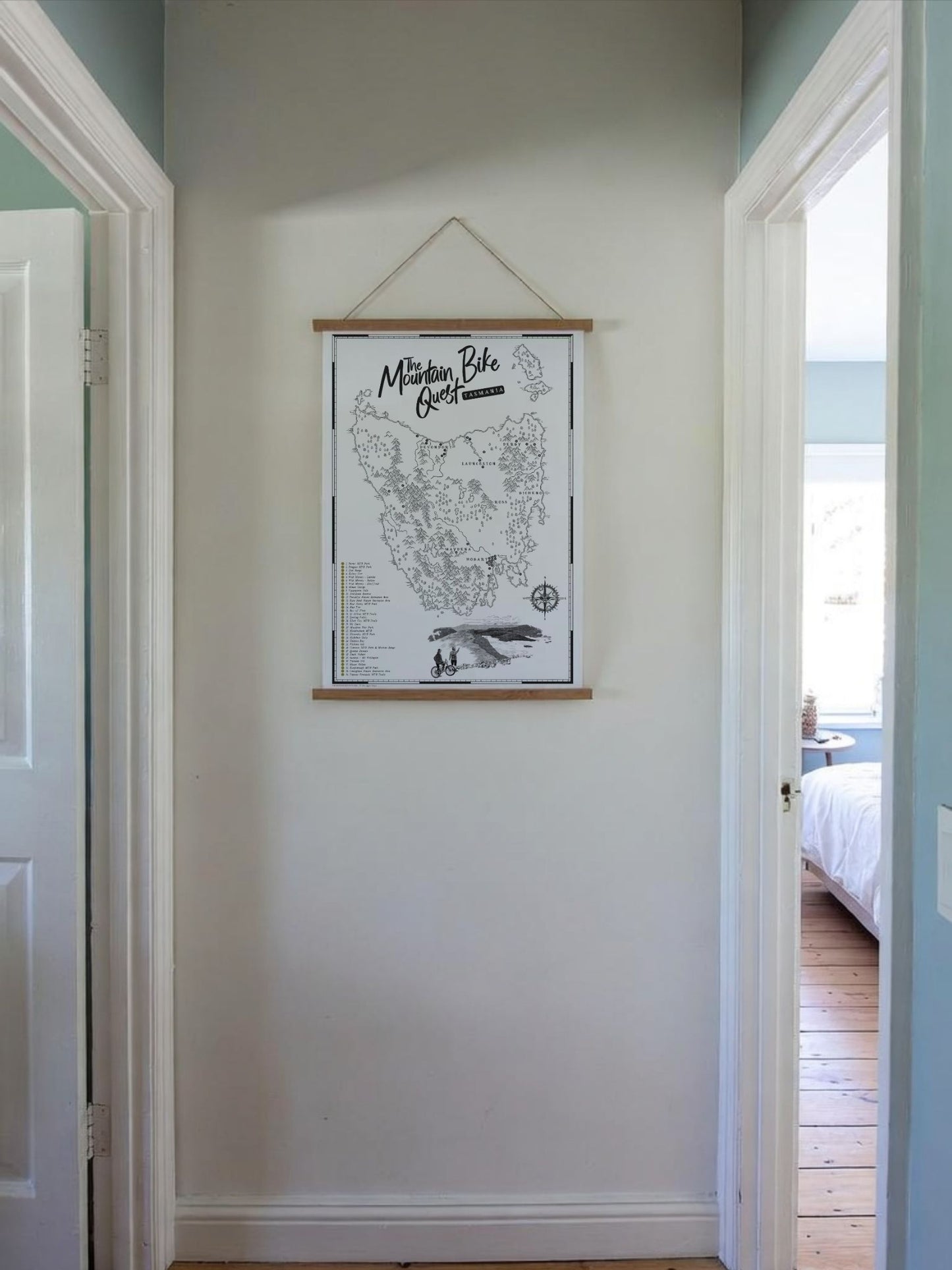 The Tasmania Mountain Bike Quest Scratch Map hanging in a wooden frame, in a hallway