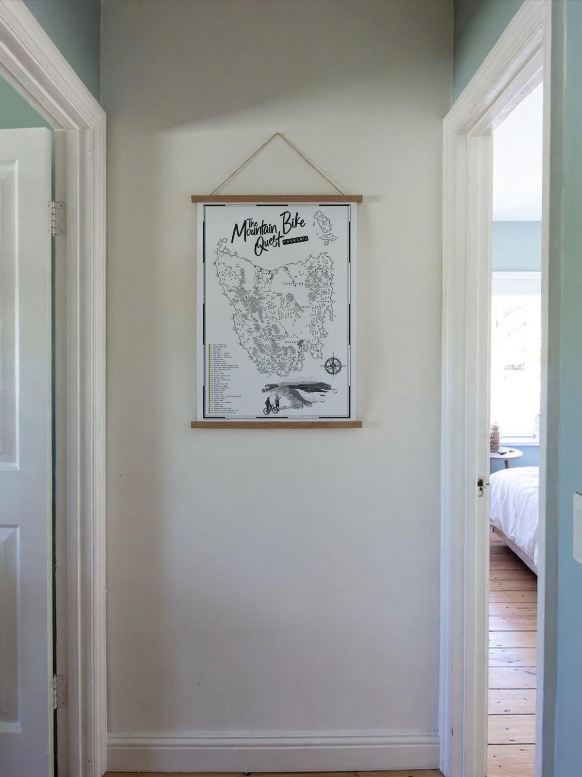 The Tasmania Mountain Bike Quest Scratch Map hanging in a wooden frame, in a hallway