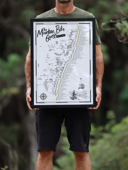 Person holding a framed NSW & ACT Mountain Bike Quest scratch map outdoors among trees
