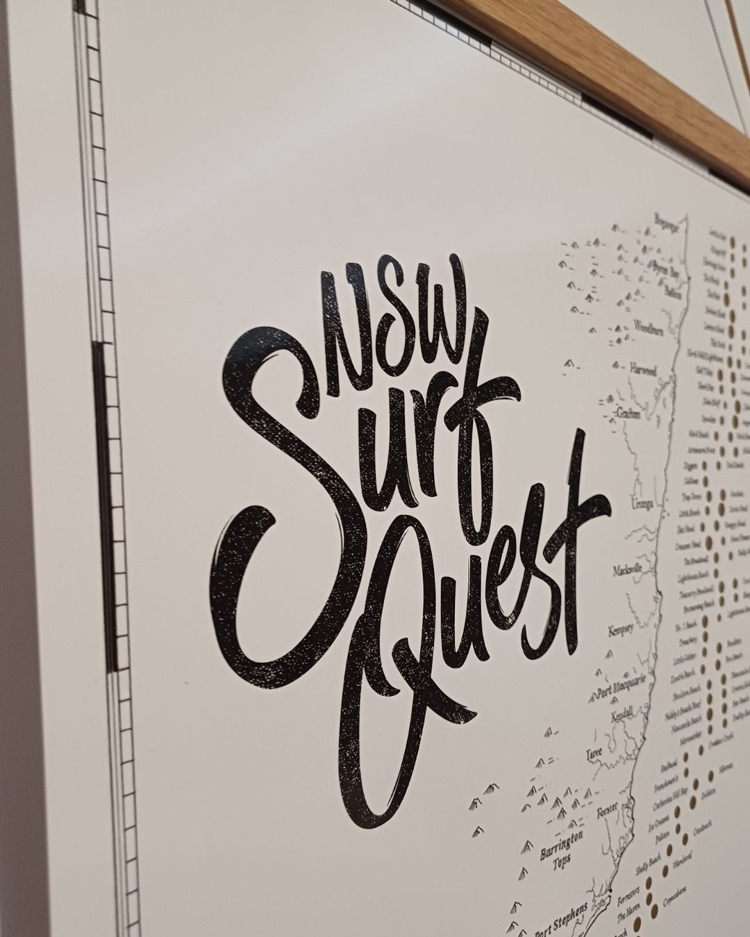Close-up of the NSW Surf Quest scratch map featuring the title, partial view of the wooden frame, and hand-drawn map, and gold scratch markers